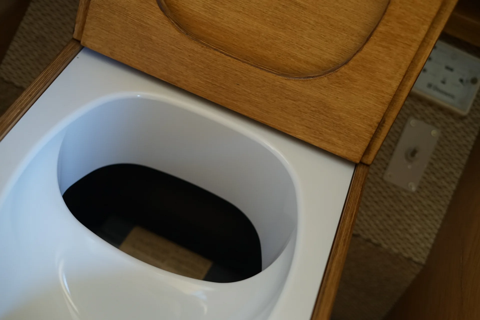 Toilettes sèches ouvertes dans un van aménagé, lunette blanche et séparateur d'urine avec le bac à litière visible