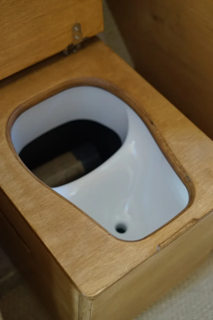 Séparateur d'urine blanc intégré au caisson de toilettes sèches, abattant en bois relevé, dans un van aménagé