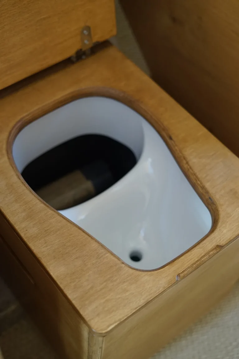 Séparateur d'urine blanc intégré au caisson de toilettes sèches, abattant en bois relevé, dans un van aménagé