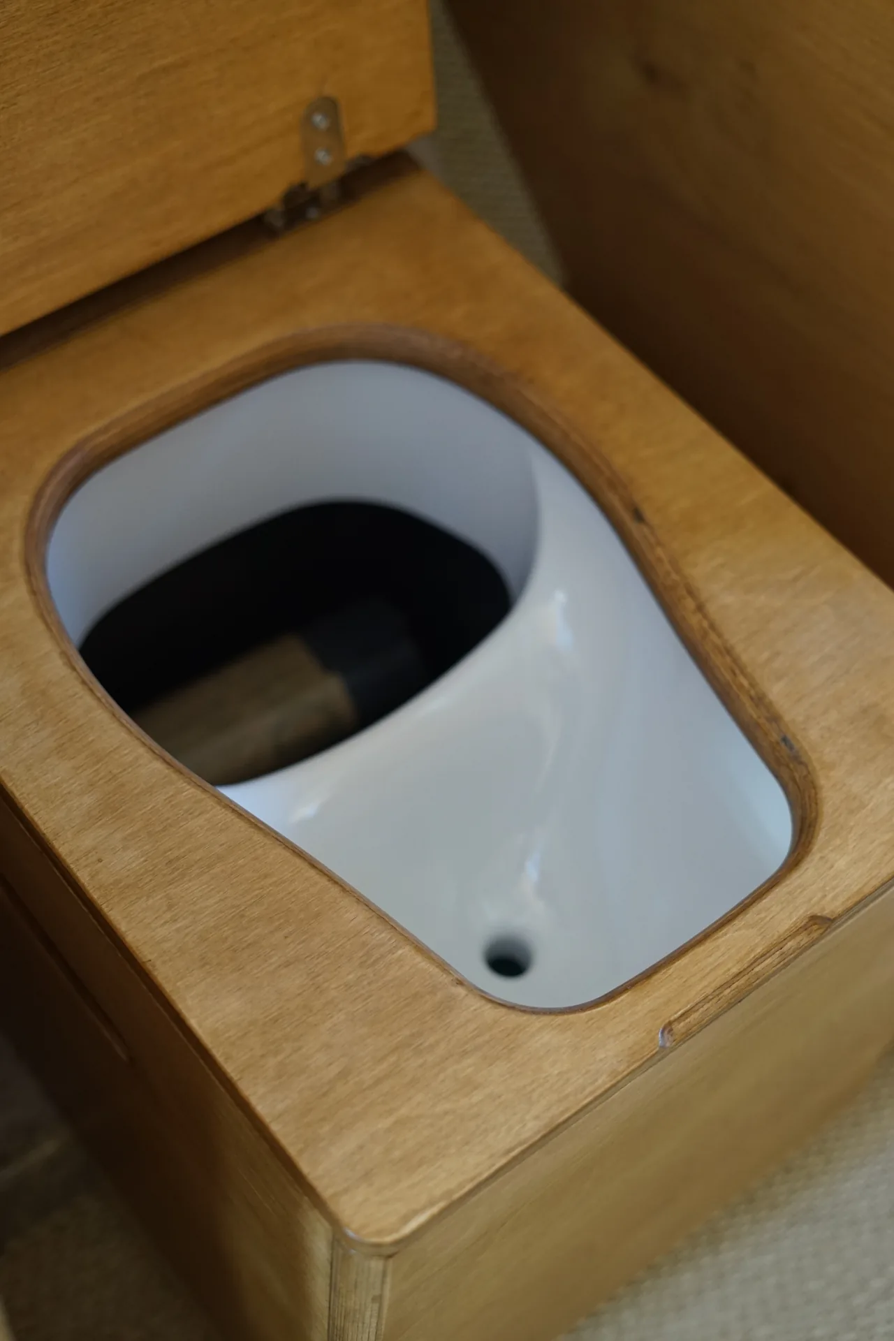 Séparateur d'urine blanc intégré au caisson de toilettes sèches, abattant en bois relevé, dans un van aménagé